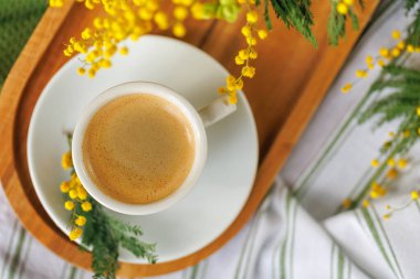 Tahta tepside sıcak bir espresso ile huzurlu bir kahve molası. Parlak mimoza çiçekleriyle süslenmiş. Taze ve ılık bir bahar hissi veriyor..