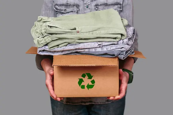 Tanınmayan bir kadın ikinci el kıyafetlerle dolu bir karton kutu tutuyor. Sürdürülebilir moda, geri dönüşüm ve hayırsever bağışları teşvik ediyor..