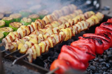 Patates dolu şişler ve kömürde ızgara yapan kırmızı biberler, yaz barbeküleri ve açık hava barbeküleri için ideal rengarenk sebzelerin rengarenk bir kombinasyonunu sergiliyor..