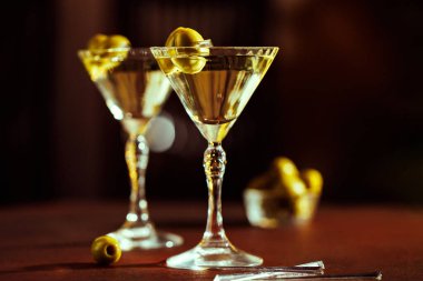 Tahta bir yüzeyde zeytinli iki martini bardağı, sıcak ve karamsar aydınlatmayla çevrili..