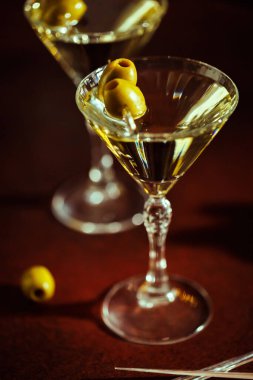 Yeşil zeytinli bir martini bardağı altın sarısı arka planda, şenlikli ve lüks bir ortam yaratıyor..