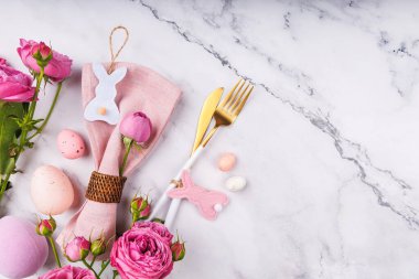 Pembe peçete, pembe gül, tavşan süsü, mermer arka planda pastel yumurta ve altın çatal bıçak seti.