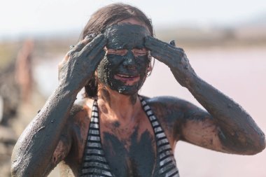 Kadın, cilt temizleme ayini sırasında alnına siyah mineral çamuru sürterek gözlerini kapatıyor...