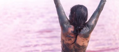 Pembe gölün önünde kollarını kaldırmış bir kadın terapatik çamur spa ritüeli sırasında