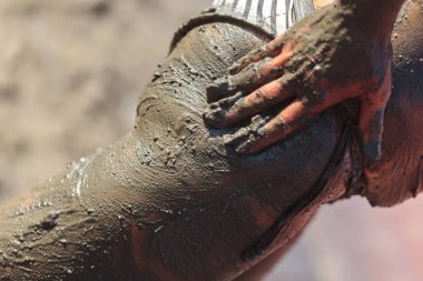 Kadın elinin kalçasına ve kalçasına doğal deri terapisi için siyah mineral çamuru sürerken yakın plan çekimi.
