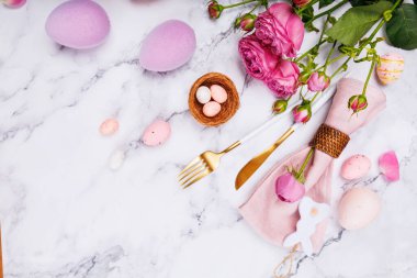 Güller, tavşan süsü, altın çatal bıçak ve mermer üzerine pastel yumurtalarla dekoratif Paskalya masası düzeni.