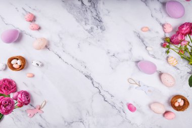Paskalya yumurtaları, pembe güller ve mermer arka planda benekli şeker yumurtaları olan mini yuvalar.
