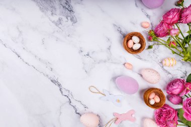 Paskalya yumurtaları, yumurta şekerli yuvaları ve süslü bahar temalı mermer arka planda pembe güller.