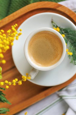 Sıcak bir bahar sabahı, bir fincan kahveyle birlikte ahşap tepside, taze mimoza çiçekleriyle çevrili, sıcak bir kahvaltı için mükemmel..
