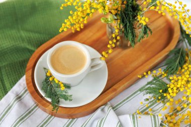 Taze sarı mimoza çiçekleriyle çevrili ahşap tepside bir fincan kahve mükemmel bir bahar sabahı atmosferi yaratır..