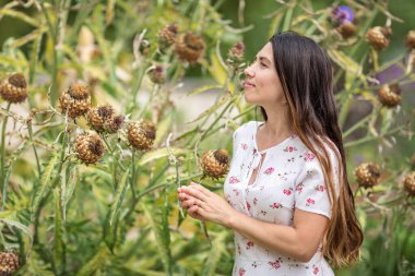 Genç ve çekici bir kadın büyük bir dulavrat otunun yanında duruyor ve yaşlı, bitkisel parktaki yapraklara dokunuyor.