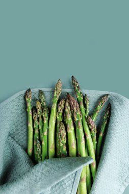 Yemek hazırlamak için pastel bir yüzey üzerinde mutfak havlusuna sarılı temiz kuşkonmaz mızraklarının üst görüntüsü.