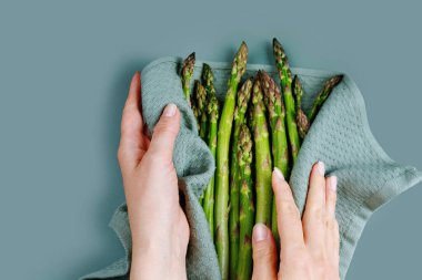 Kadının elleri, mutfak havlusuyla yeşil kuşkonmazları nazikçe kurutuyor.