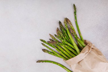 Açık seramik yüzeye sarılı kahverengi kağıtta bir demet taze kuşkonmaz.