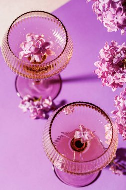 Üzerinde leylak çiçekleriyle süslenmiş ve mor yüzeyde buketlerle çevrili şampanya kadehleri var.