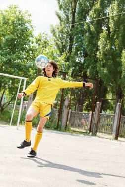 Sarı spor üniformalı genç, şehir dışında futbol oynuyor.