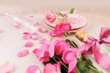 Taze pembe güller, dağınık yapraklar, şampanya şişesi ve yumuşak pastel yemek takımlarıyla hassas bir düzenleme..