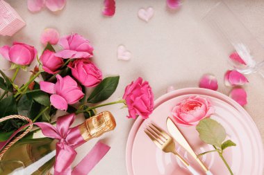 İçinde pembe tabaklar, taze güller, kurdeleli şampanya şişesi ve dağınık gül yaprakları olan şık bir masa..