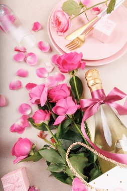 Zarif bir Sevgililer Günü masası pembe güller, yaylı bir şampanya şişesi dağınık yapraklar ve zarif sofra takımı..