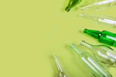 Görsel geri dönüşüm için açık yeşil zemin üzerinde boşlukla düzenlenmiş çoklu yeşil ve berrak cam şişeler