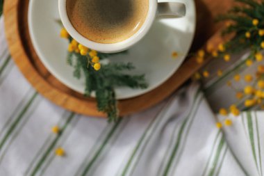 Tahta tepside mimoza çiçekleri olan bir kahve fincanının yukarıdan aşağı görüntüsü sıcak ve samimi bir atmosfer yaratıyor..