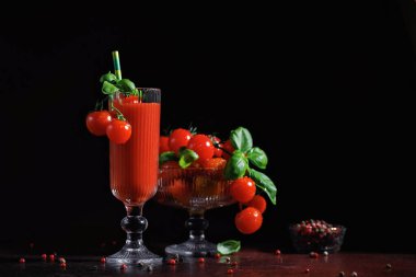 Fesleğen ve kiraz domatesli cam bardakta taze domates kokteyli dramatik ışıklandırmalı, kırsal karanlık bir masada.