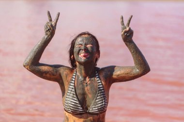 Çamura bulanmış, kafasının yanında barış işareti yapan ve dilini dışarı çıkaran bir kadın.