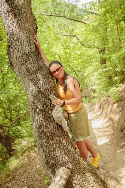 Orman yolunda yürüyen ve akıllı telefon kullanan bir kadın. Çekici kadın gezgin yürüyüş yolunda rahatlıyor ve doğanın tadını çıkarıyor.