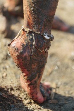 Topuğu ve bileği mineral çamura bulanmış, kumlu sahilde dekoratif deniz halhalı takılı.