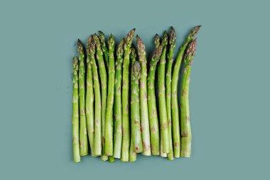 Sağlıklı yemek ve hazırlık için yukarıdan bakıldığında mavi bir yüzeyde düzgün sıralanmış yeşil kuşkonmaz sapları.