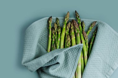 Taze yeşil kuşkonmaz mızrakları mavi yüzeyde dokulu bir havluyla kurutuluyor.