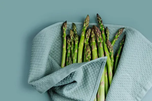 Taze yeşil kuşkonmaz mızrakları mavi yüzeyde dokulu bir havluyla kurutuluyor.