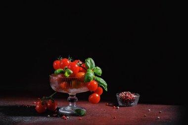 Olgun kiraz domatesleri ve kaburgalı tatlı kasesinde taze fesleğen. Etrafı koyu dokulu baharatlarla çevrili.