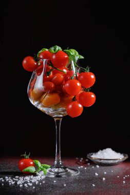Fesleğenli kırmızı kiraz domatesleri, koyu arka planda tuzla çevrili, gurme temiz yemek ve sağlıklı yemekler için yaşam konsepti.