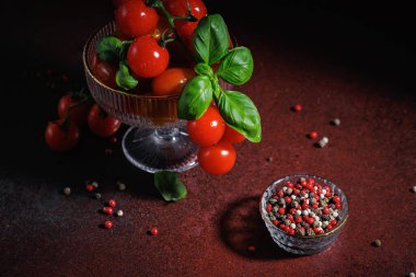 Canlı kırmızı kiraz domatesleri ve fesleğen yaprakları. Kırsal bir yüzeyde kristal bir kasede şekillendirilmiş. Vegan ve temiz yiyecekler için ideal.