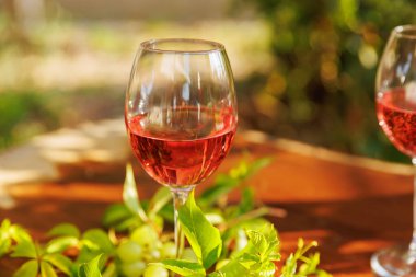 Beyaz üzümlü bir bardak gül şarabı ve açık havada, ahşap masada yeşil yapraklar.