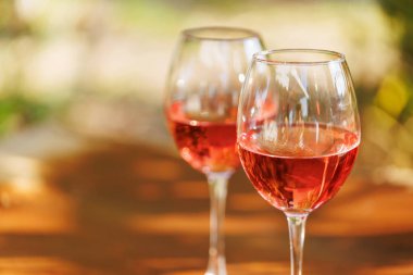 İki bardak dolusu gül şarabı, ahşap masanın üzerinde. Yatay kompozisyonda, yumuşak güneş ışığıyla birlikte.