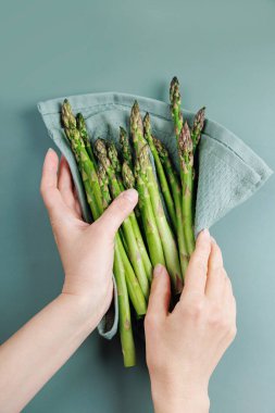 Kadın ellerinin mutfak havlusuna sarılı taze kuşkonmaz tutuşu.