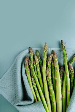 Pastel yüzeyde mutfak havlusuna sarılı taze kuşkonmazın dikey üst görüntüsü.