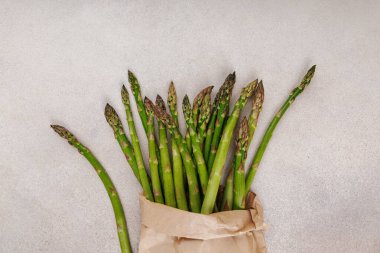 Yumuşak seramik arkaplan üzerine kahverengi kağıt sarılı yeşil kuşkonmaz saplarını kapat, üst görünüm