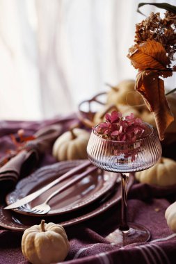 Beyaz balkabaklı güzel bir sonbahar yemek masası, desenli bir keten peçete, örülmüş bir peçete halkası ve kaliteli bir kadeh, rahat ve şenlikli bir atmosfer yaratıyor.