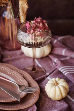 Kaliteli bir sonbahar sofra düzeninin yakın çekimi klasik tabaklar, kurumuş çiçeklerle dolu yumuşak bir keten peçete ve bol desenli masa örtüsüne yerleştirilmiş çatal bıçak takımı, mevsimlik dekorasyon için mükemmel.