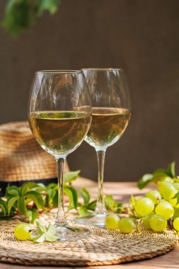 Beyaz şarap kadehleri ve asma yaprakları saman şapka ve güneş ışığıyla ahşap yüzeyde..