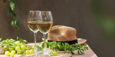 Yaz verandasında saman şapkalı ve yeşil yapraklı iki şarap kadehi ve taze üzüm...