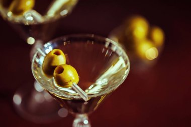 Zeytinli bir martini bardağının dramatik yakın çekimi loş bir bardaki ılık ışığı yansıtıyor..