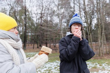 Donmuş ellere üfleyen ergen anne, doğa yürüyüşü sırasında sıcak eldivenler sunuyor.