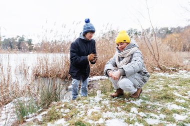 Kış manzarasında küçük bir kardan adam yapan anne, genç oğlunun yakından izlediği samimi bir an.