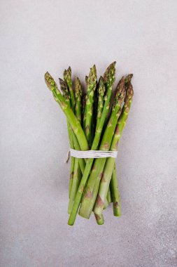 Bir demet yeşil kuşkonmaz buket gibi dizilmiş ve iple bağlanmış, tarafsız arka planda duruyor. Sağlıklı beslenme, vejetaryen yemekleri ve ekolojik yaşam tarzı kavramı.