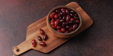 Olgun kornelian kirazlarının, ahşap bir tahta kesme tahtasındaki ahşap bir kasede yakın plan çekimi. Mevsimlik organik meyveler sağlıklı yemek ve ev yapımı tarifler için hazır..