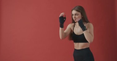 Güçlü, zayıf bir sporcunun çalışması, ısınması, boks yapması, tekme atması, bacak kaldırması. Güzel, sportif kadın eğitimi, egzersiz. Kırmızı stüdyo arka planında izole edilmiş..